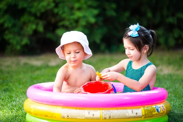 Subject childhood summer games in the yard. Caucasian brother and sister playing plastic toys bucket sitting in the water, inflatable round children\'s pool. Summer is hot, rest in swimsuits
