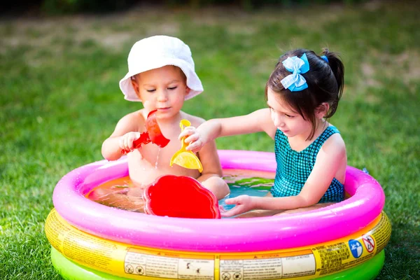 Subject childhood summer games in the yard. Caucasian brother and sister playing plastic toys bucket sitting in the water, inflatable round children\'s pool. Summer is hot, rest in swimsuits