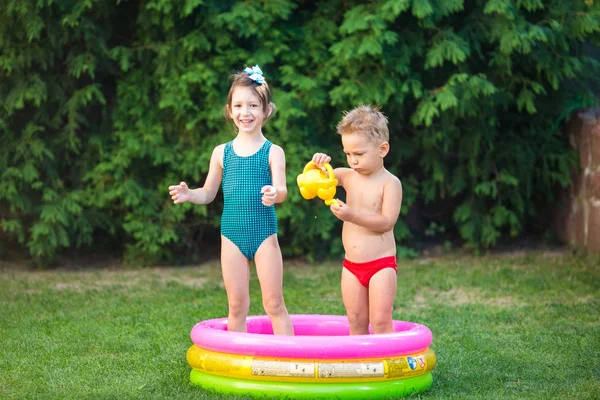 Su havuzu ile çocukluk yaz oyunları. Kafkas erkek ve kız kardeşi plastik oyuncaklar sulama ile oynamak su sıçraması, şişme yuvarlak çocuk banyo dökebilirsiniz. Mayolarla yaz sıcak tatilleri — Stok fotoğraf