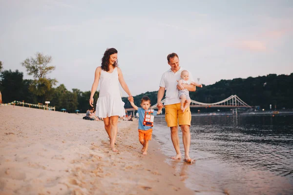 Family vacation in summer. Young Caucasian family foot walking barefoot sandy beach, shore river water. Dad mom holding hands two children, brothers. Big friendly family with two children near lake — Stock Photo, Image