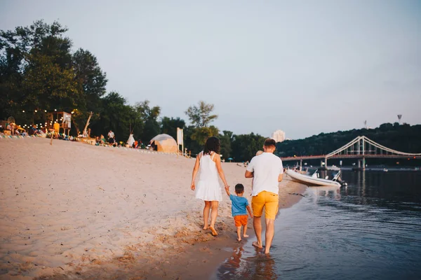 Vacaciones familiares en verano. Joven familia caucásica pie caminando descalzo playa de arena, ribera de agua del río. Papá mamá cogido de la mano dos hijos, hermanos. Gran familia amigable con dos niños cerca del lago —  Fotos de Stock