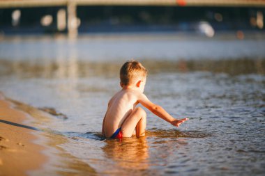 Tema yaz saati ve su yakınında dinlenme. Küçük neşeli Kafkas komik çocuk oynar ve nehirde sahiptir. Çocuk dinleniyor ve göl gölet kumlu plajda yüzüyor