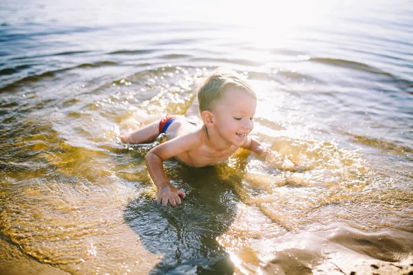 Тема летнего времени и отдыха у воды. Маленький веселый кавказский юморист играет и наслаждается в реке. Ребенок отдыхает и плавает в озере пруд песчаный пляж — стоковое фото