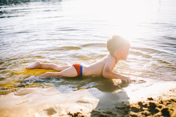 Тема летнего времени и отдыха у воды. Маленький веселый кавказский юморист играет и наслаждается в реке. Ребенок отдыхает и плавает в озере пруд песчаный пляж — стоковое фото