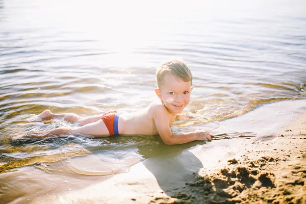 Thema ist die Sommerzeit und die Ruhe am Wasser. kleiner fröhlicher kaukasischer lustiger Junge spielt und genießt im Fluss. das Kind ruht sich aus und schwimmt im Teich — Stockfoto