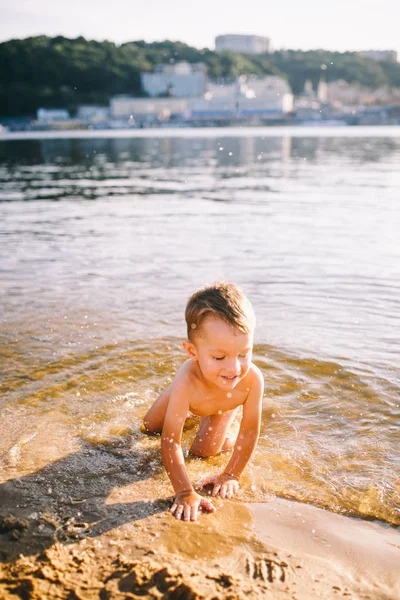 Le thème est l'heure d'été et de repos près de l'eau. Petit garçon drôle caucasien joyeux joue et aime dans la rivière. L'enfant se repose et nage dans l'étang du lac plage de sable — Photo