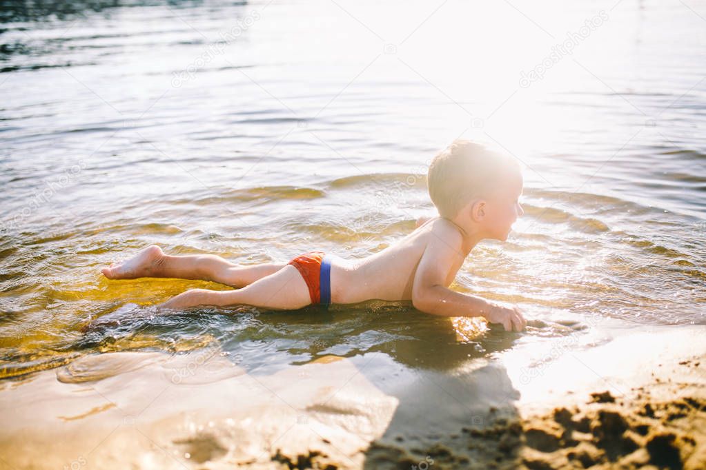 Theme is summer time and rest near the water. Little joyful Caucasian funny boy plays and enjoys in the river. The child is resting and swimming in the lake pond sandy beach