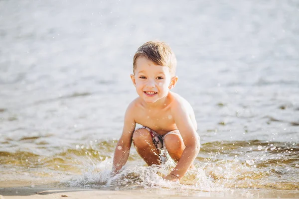 Tema es la hora de verano y el descanso cerca del agua. Poco alegre caucásico divertido chico juega y disfruta en el río. El niño está descansando y nadando en la playa de arena lago estanque —  Fotos de Stock