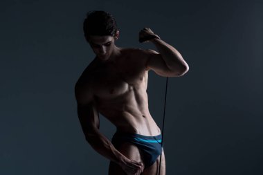 Kas Fitness genç erkek antika mükemmel kaslar altı paketleri ABS ve çıplak göğüs. Stüdyodan karanlık bir arka plana karşı streç elastik ile vücut geliştirmeci Model trenler. Egzersiz eğitim spor salonu