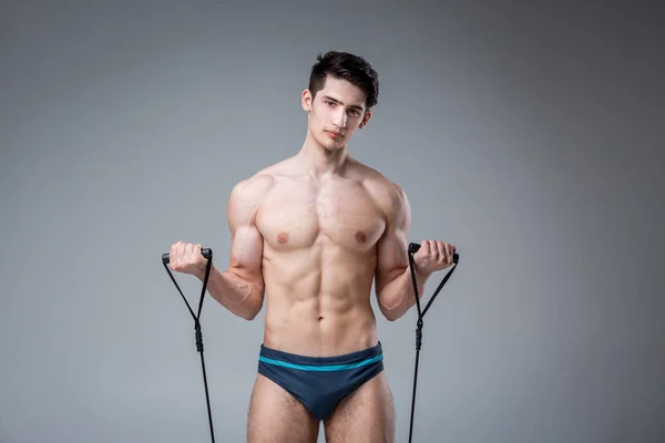Muscular fitness young male antique perfect muscles six packs of abs and bare chest. Bodybuilder model trains with a stretching elastic against a dark background in the studio. Workout training gym