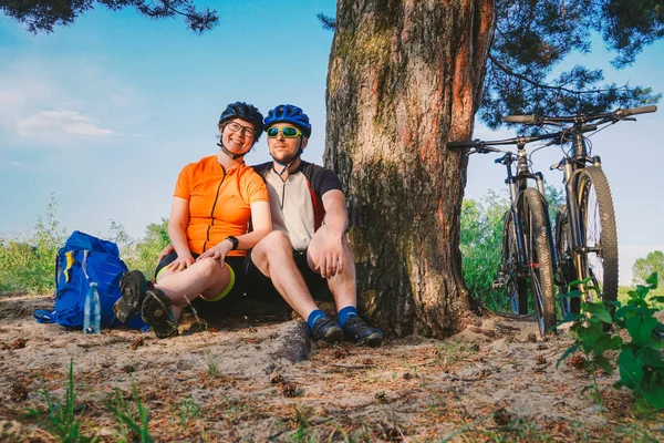 Szczęśliwa para z rowerem górskim siedzieć obejmując charakter rekreacyjny na zewnątrz. szczęśliwa para, prowadzić aktywny tryb życia, zatrzymał się w lesie w pobliżu drzewa zrobić sobie przerwę. Sport tematyczny i aktywny styl życia i romans — Zdjęcie stockowe