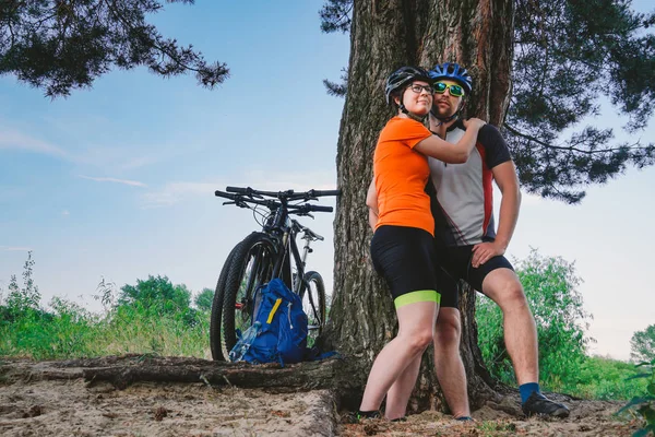 Ευτυχισμένο ζευγάρι με ποδήλατο βουνού αγκαλιάζοντας φύση αναψυχής σε εξωτερικούς χώρους. ευτυχισμένο ζευγάρι, να οδηγήσει έναν δραστήριο τρόπο ζωής, σταμάτησε στο δάσος κοντά δέντρο κάνει ένα διάλειμμα. Θεματικά αθλήματα και ενεργός τρόπος ζωής και ρομαντισμός — Φωτογραφία Αρχείου