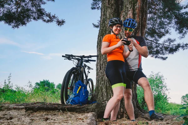 Szczęśliwa para szuka na mapie w celu smartphone. mężczyzna i kobieta w hełmach podróżujących rowerem górskim po trudnym terenie. Turystyka tematyczna i nawigacja, sposób wyszukiwania, Tworzenie trasy, aplikacja telefonu GPS — Zdjęcie stockowe