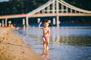Kiev Ukrayna 'da şehir plajında nehrin yakınında tema yaz açık hava etkinlikleri. Nehir kıyısında çalışan küçük komik bebek çocuk, su kumlu plaj yaz saati bir sıçrama atlama