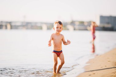 Kiev Ukrayna 'da şehir plajında nehrin yakınında tema yaz açık hava etkinlikleri. Nehir kıyısında çalışan küçük komik bebek çocuk, su kumlu plaj yaz saati bir sıçrama atlama