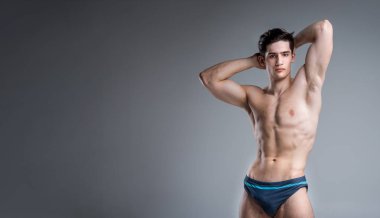 Genç Erkek atlet vücut geliştirmeci poz. Yakışıklı atletik erkek güç adam. Fitness kas kişi. Stüdyoda kaslar gösteren genç atlet. altı paket kasları gri arka planda gömleksiz poz