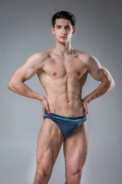Νέος αρσενικός αθλητής bodybuilder που ποζάρει. Ωραίος αθλητικός άντρας με δύναμη. Γυμνασμένο πρόσωπο. Νέος αθλητής που δείχνει μύες στο στούντιο. έξι πακέτα μύες που θέτουν ημίγυμνοι σε γκρι φόντο — Φωτογραφία Αρχείου
