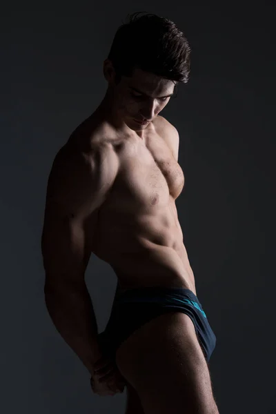 Jovem atleta masculino fisiculturista posando. Bonito atlético do sexo masculino. Aptidão muscular pessoa. Jovem atleta mostrando músculos no estúdio. seis pacotes de músculos posando sem camisa no fundo cinza — Fotografia de Stock