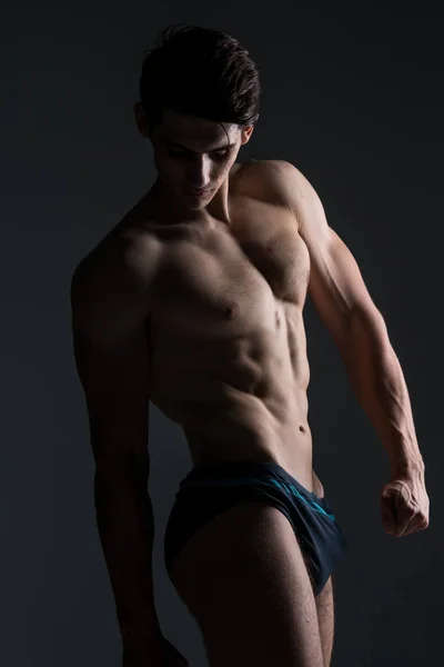Νέος αρσενικός αθλητής bodybuilder που ποζάρει. Ωραίος αθλητικός άντρας με δύναμη. Γυμνασμένο πρόσωπο. Νέος αθλητής που δείχνει μύες στο στούντιο. έξι πακέτα μύες που θέτουν ημίγυμνοι σε γκρι φόντο — Φωτογραφία Αρχείου