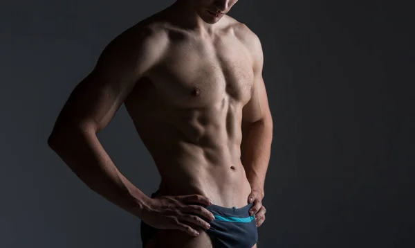 Jovem atleta masculino fisiculturista posando. Bonito atlético do sexo masculino. Aptidão muscular pessoa. Jovem atleta mostrando músculos no estúdio. seis pacotes de músculos posando sem camisa no fundo cinza — Fotografia de Stock