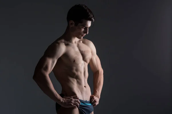 Jovem atleta masculino fisiculturista posando. Bonito atlético do sexo masculino. Aptidão muscular pessoa. Jovem atleta mostrando músculos no estúdio. seis pacotes de músculos posando sem camisa no fundo cinza — Fotografia de Stock