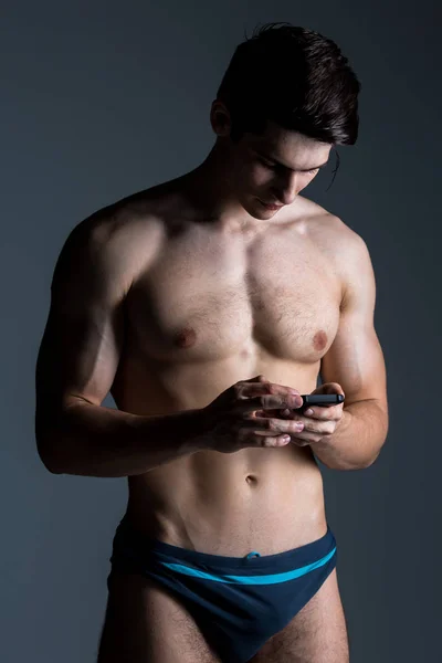 Baixo retrato chave do homem sem camisa muscular no fundo escuro de pé com telefone inteligente — Fotografia de Stock