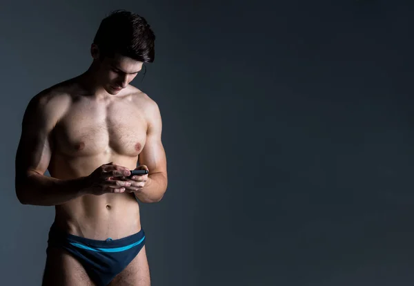 Basso ritratto chiave di uomo muscoloso senza maglietta a sfondo scuro in piedi con smart phone — Foto Stock