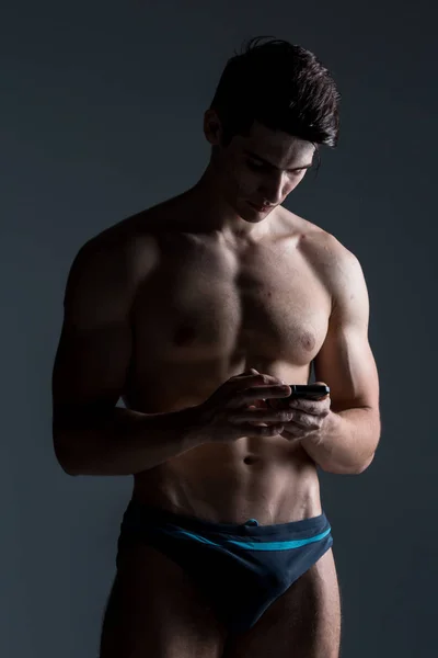 低键肖像肌肉无衬衫的人在黑暗的背景站在智能手机 — 图库照片