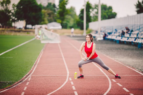 Esportes fitness mulheres caucasianas fazendo aquecimento antes do exercício. Atleta esticar as pernas fazendo aquecimento antes do treinamento. Jogging na cidade no estádio. Menina usa fone de ouvido telefone sportswear — Fotografia de Stock