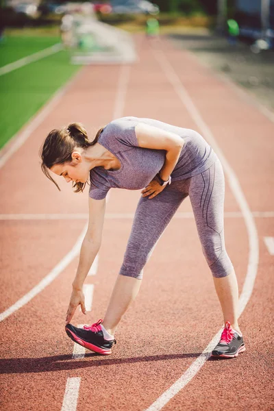 Portrait Of A Beautiful Young Caucasian Woman With Long Hair In The Tail  And Big Breasts Posing In Gray Sportswear Standing Training On A Running  Stadium, A Red Rubber Track In Summer