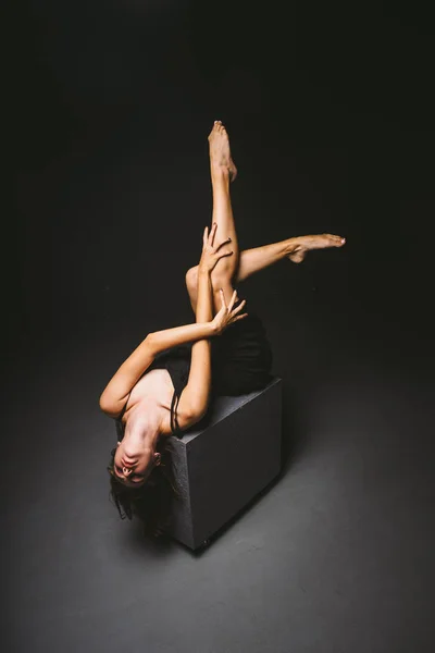 Tema social. jovem mulher caucasiana em pose estranha em vestido posando no cubo preto, fundo escuro, simboliza dor, sofrimento, buscando ajuda, proteção de uma sociedade má. Arte moderna, abstração — Fotografia de Stock