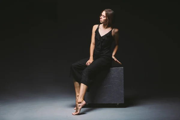 Young Caucasian female model posing in studio black background.Girl sitting in a black dress on a dark wall. Subject severe poor psychological state, intra, problems, personality conflict