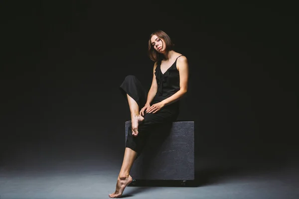 Young Caucasian female model posing in studio black background.Girl sitting in a black dress on a dark wall. Subject severe poor psychological state, intra, problems, personality conflict — 스톡 사진