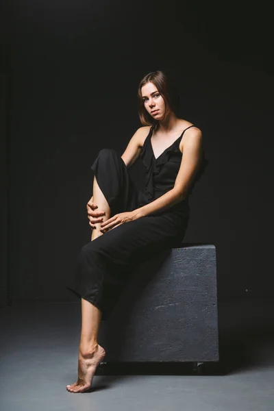 Young Caucasian female model posing in studio black background.Girl sitting in a black dress on a dark wall. Subject severe poor psychological state, intra, problems, personality conflict