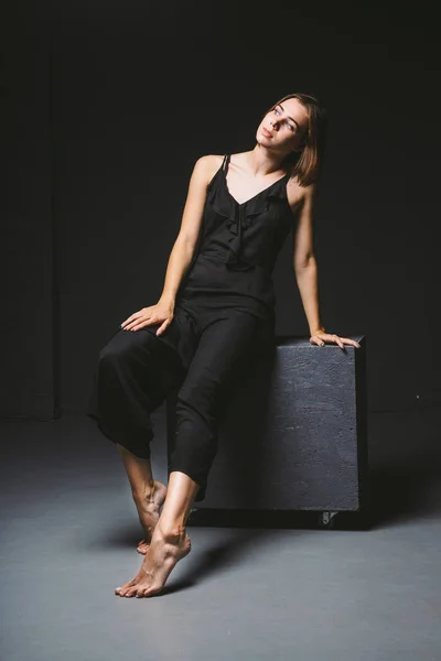 Young Caucasian female model posing in studio black background.Girl sitting in a black dress on a dark wall. Subject severe poor psychological state, intra, problems, personality conflict