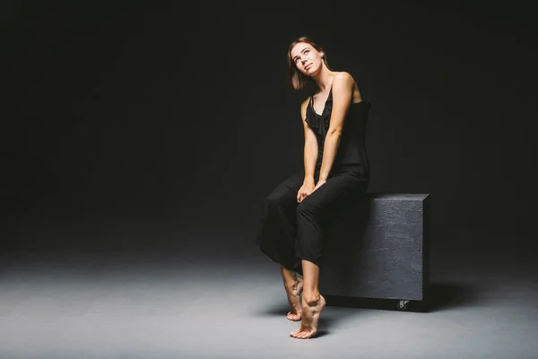 Young Caucasian female model posing in studio black background.Girl sitting in a black dress on a dark wall. Subject severe poor psychological state, intra, problems, personality conflict — 스톡 사진