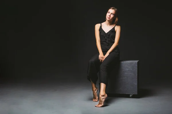 Young Caucasian female model posing in studio black background.Girl sitting in a black dress on a dark wall. Subject severe poor psychological state, intra, problems, personality conflict — 스톡 사진
