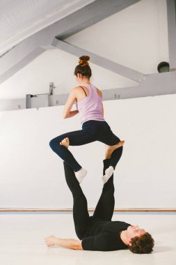 Genç çift birlikte spor salonunda bir paspas üzerinde akroyoga pratik. Kadın uçar. Erkek ve kadın spor eğitim akrobasi yoga içinde. Affiliate yoga, esneklik, güven kavramı. Takım çalışması