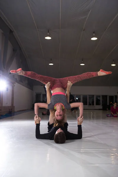 Молода пара практикує акройогу на килимку в спортзалі разом. Жінка летить. Чоловік і жінка спортивні тренування акробатики йоги всередині. Партнерська йога, гнучкість, концепція довіри. Командна робота — стокове фото