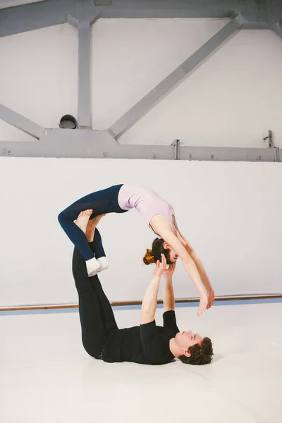 Pareja joven practicando akroyoga en una esterilla en el gimnasio juntos. La mujer vuela. Hombre y mujer de entrenamiento deportivo acrobacias yoga en el interior. Yoga afiliado, flexibilidad, concepto de confianza. Trabajo en equipo — Foto de Stock