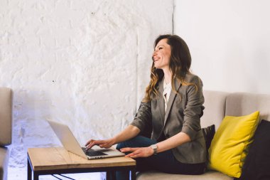 İş yerinde konsantre oldu. Kendine güvenen genç yetişkin orta yaşlı kadın akıllı rahat giysiler içinde, bir dizüstü bilgisayar üzerinde çalışan, yaratıcı bir ofis veya kafe içinde oturan. Tema iş kadını boş alanda çalışmak