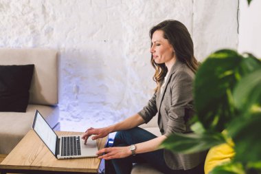 İş yerinde konsantre oldu. Kendine güvenen genç yetişkin orta yaşlı kadın akıllı rahat giysiler içinde, bir dizüstü bilgisayar üzerinde çalışan, yaratıcı bir ofis veya kafe içinde oturan. Tema iş kadını boş alanda çalışmak