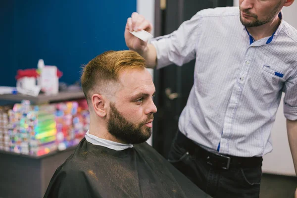 Barber Making Haircut Bearded Man In Barbershop. Professional stylist cutting client hair in salon. Barber using scissors and comb. Skillful hairdresser cutting male hair. Hair Care Service Concept — Stock Photo, Image