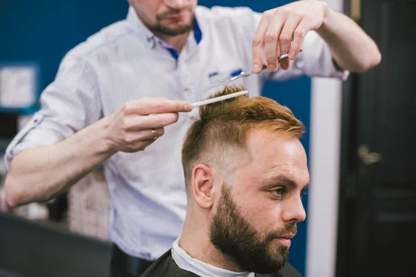 理髪店で髪を切るひげの男を作る床屋。サロンでクライアントの髪をカットプロのスタイリスト。はさみと櫛を使った床屋。男性の髪を切断する巧みな美容師。ヘアケアサービスコンセプト — ストック写真
