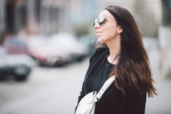 Retrato de uma jovem bela mulher caucasiana no fundo da rua. Menina modelo com cabelos longos e óculos de sol com reflexão posando em roupas pretas em um ambiente urbano — Fotografia de Stock