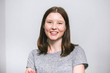 beyaz stüdyo arka plan üzerinde gri t-shirt gülümseyen şık genç güzel Kafkas kadın portresi, izole, doğal bir görünüm, uzun kahverengi saçlı