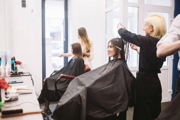 Peluquería sosteniendo tijeras y peine y hace que la mujer corte de pelo cliente. Joven hermosa mujer corte de pelo en el salón de belleza. Proceso de corte de cabello con tijeras de uso. Peluquería recorte marrón. —  Fotos de Stock