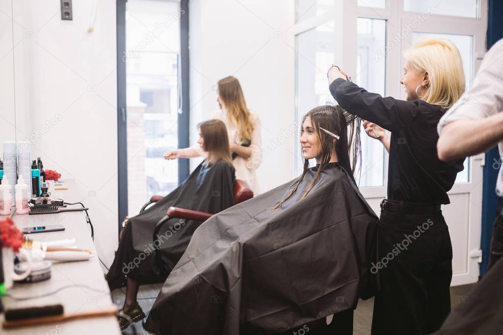 hairdresser holding scissors and comb and makes haircut woman client. Young beautiful woman hair cut in beauty salon. Process of hair cutting with use scissors. Hairdresser trimming brown.