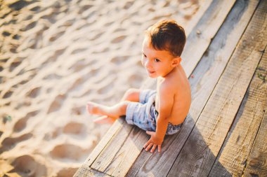 Küçük Kafkas çocuk ahşap iskele kumlu plajda oturan, yaz saati, su yakınında deniz tatili. Tema zamanın akışı, kısa bir yaşam, varlığın anlamı ve amacıdır. Hayatın anlamı