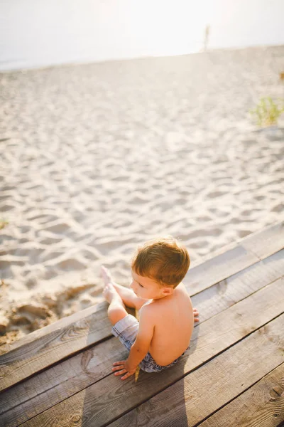 Niño pequeño caucásico sentado en la playa de arena del muelle de madera, hora de verano, vacaciones de mar cerca del agua. El tema es el flujo del tiempo, una vida corta, el significado y el propósito de la existencia. Significado de la vida —  Fotos de Stock